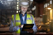 Male engineer working at glowing digital tablet in dark factory — Stock Photo