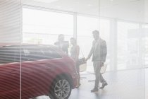 Vendeur de voiture montrant la nouvelle voiture aux clients dans la salle d'exposition de concession de voiture — Photo de stock
