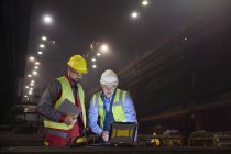 Steelworkers usando laptop em moinho de aço escuro — Fotografia de Stock