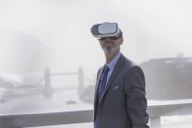 Uomo d'affari che utilizza occhiali simulatore di realtà virtuale sul ponte urbano soleggiato sul Tamigi, Londra, Regno Unito — Foto stock