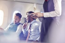 Flight attendant serving champagne to businessmen in first class on airplane — Stock Photo