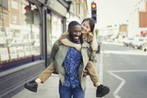 Giocoso giovane coppia piggybacking su strada urbana — Foto stock