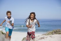 Playful brother and sister running on sunny summer ocean beach — Stock Photo