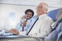 Lächelnde Geschäftsleute tauschen im Flugzeug Visitenkarten aus — Stockfoto