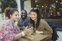Молодые друзья используют мобильный телефон в кафе на тротуаре — стоковое фото