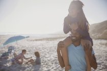 Lächelnder Vater trägt Tochter auf Schultern am sonnigen Sommerstrand — Stockfoto