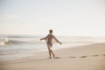 Беззаботная женщина ходит с распростертыми руками на солнечном летнем пляже океана — стоковое фото
