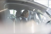 Smiling female customer sitting in driver?s seat of new car in car dealership — Stock Photo