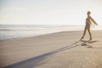 Беззаботная женщина гуляет по солнечному летнему океанскому пляжу — стоковое фото