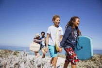 Familia caminando con boogie boards en soleado sendero de playa de verano - foto de stock