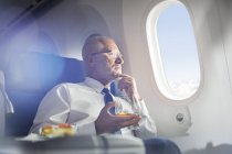Старший бізнесмен п'є віскі першого класу, дивлячись на вікно літака — стокове фото