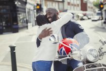Affectionate young couple hugging at motor scooter on sunny urban street — Stock Photo