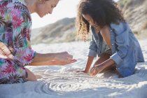 Mother and daughter drawing spirals in sand on summer beach — Stock Photo