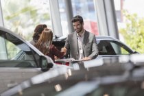 Car salesman handshaking with customers in car dealership showroom — Stock Photo