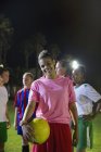 Portrait smiling, confident young female soccer player with ball on field at night — Stock Photo