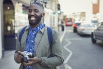 Усміхнений молодий турист-чоловік з камерою на міській вулиці — стокове фото