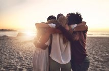 Jovens amigos abraçando em um aconchego na praia de verão por do sol — Fotografia de Stock