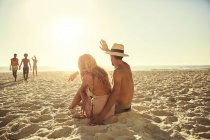 Молода пара махає друзям на сонячному літньому пляжі — стокове фото