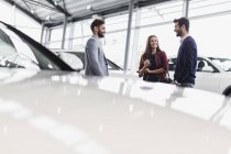 Vendedor de carros conversando com clientes casal no showroom concessionária de automóveis — Fotografia de Stock