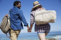 Многонациональная пара, держащаяся за руки, гуляющая по солнечному летнему океанскому пляжу — стоковое фото