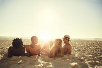 Young couples laying, relaxing on sunny summer beach — Stock Photo
