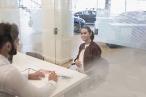Car salesman talking to pregnant customer in car dealership office — Stock Photo