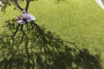 Businesswoman working on blanket below tree in sunny yard — Stock Photo