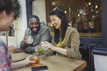 Sonrientes jóvenes amigos bebiendo jugo en el café de la acera - foto de stock