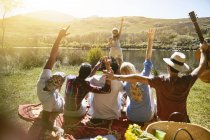 Женщина с фотоаппаратом фотографирует друзей с поднятыми на солнечном берегу летом руками — стоковое фото
