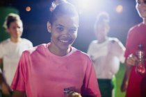 Portrait confident young female soccer player on field with teammates at night — Stock Photo