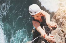 Determinada, focada mulher alpinista pendurada na rocha acima do oceano ensolarado — Fotografia de Stock