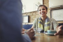 Mujer joven sonriente hablando con un amigo, tomando café en la mesa del café - foto de stock