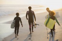 Famille multi-ethnique portant des planches de surf et de boogie sur la plage ensoleillée du coucher du soleil d'été — Photo de stock