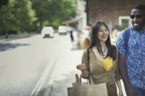 Улыбающаяся молодая пара с сумкой для покупок ходит по тротуару — стоковое фото