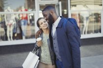 Affectionate young couple with coffee and shopping bag outside storefront — Stock Photo