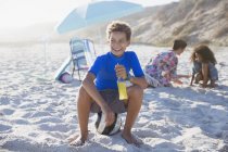 Sonriente niño bebiendo jugo en la soleada playa de verano - foto de stock