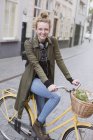 Portrait smiling young woman with headphones riding bicycle with produce in basket — Stock Photo