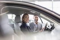 Portrait femme souriante et vendeur de voitures assis dans une voiture neuve chez le concessionnaire automobile — Photo de stock