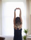 Frau übt Yoga, streckt Arme über Kopf am Fenster aus — Stockfoto