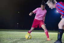 Young female soccer players playing on field at night, kicking the ball — Stock Photo