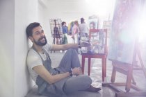 Retrato sorridente artista masculino com pintura em paleta no cavalete em estúdio de classe de arte — Fotografia de Stock