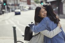 Усміхнені лагідні друзі-жінки обіймаються на сонячній міській вулиці — стокове фото