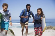 Familia juguetona con boogie board corriendo en la soleada playa de verano - foto de stock