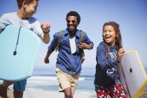 Счастливый отец и дети с буги-бордами, бегущими по солнечному летнему пляжу — стоковое фото