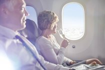 Женщина пьет шампанское в первом классе, смотрит в окно самолета — стоковое фото