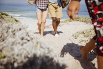 Jambes de couple multi-ethnique marchant sur le sentier ensoleillé de la plage de sable d'été — Photo de stock