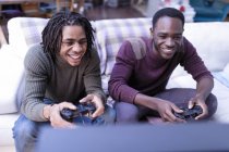 Sonrientes hermanos jugando videojuegos en el sofá - foto de stock