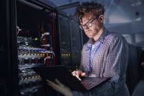 Técnico de TI masculino enfocado que trabaja en la computadora portátil en la sala de servidores oscuros - foto de stock