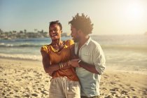 Verspieltes junges Paar umarmt und lacht am sonnigen Sommerstrand am Meer — Stockfoto