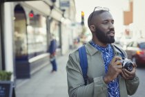 Joven turista masculino fotografiando con cámara en calle urbana - foto de stock